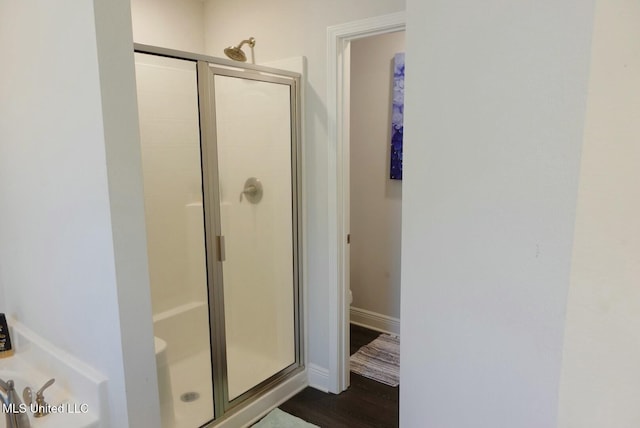 bathroom with toilet, a shower stall, baseboards, and wood finished floors