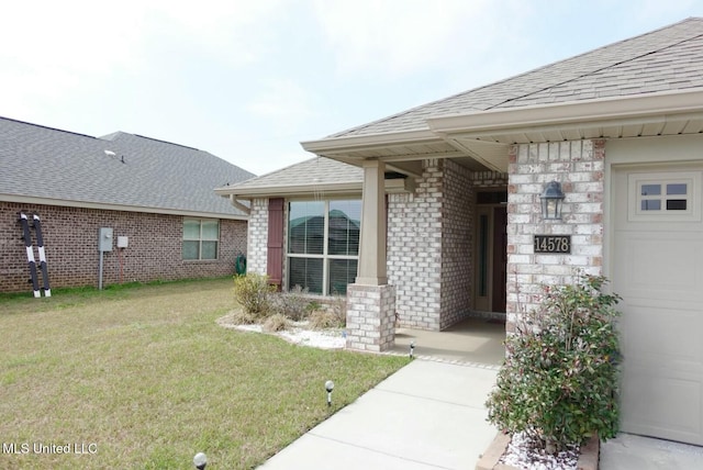 property entrance featuring a garage, roof with shingles, a lawn, and brick siding