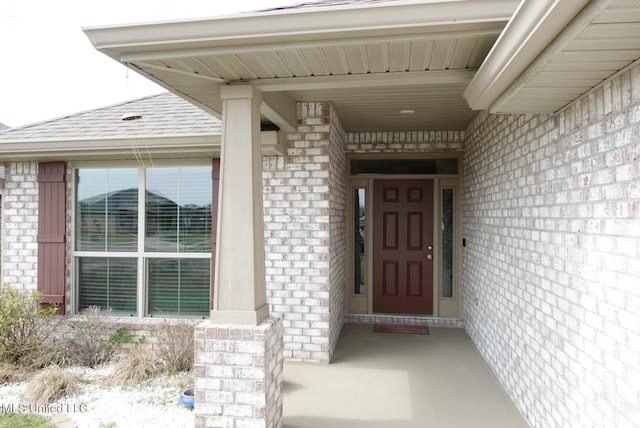 entrance to property with a shingled roof and brick siding