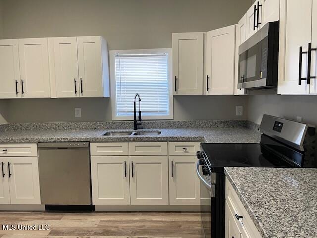 kitchen featuring light wood-type flooring, stainless steel appliances, light stone countertops, white cabinets, and sink