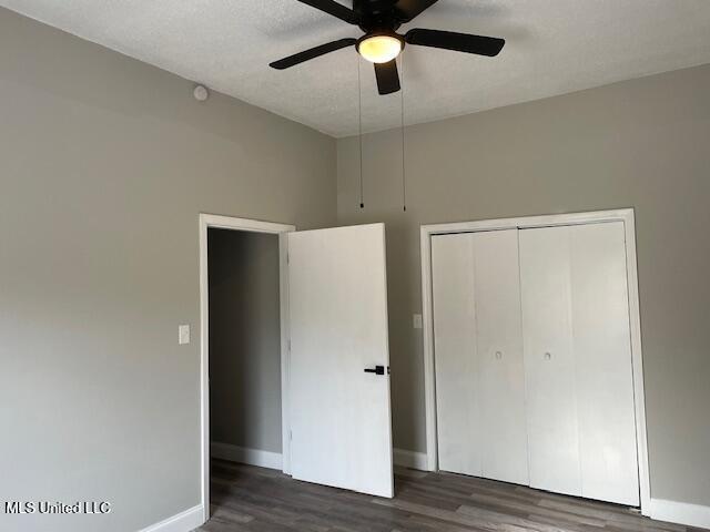 unfurnished bedroom with ceiling fan, dark wood-type flooring, a textured ceiling, and a closet