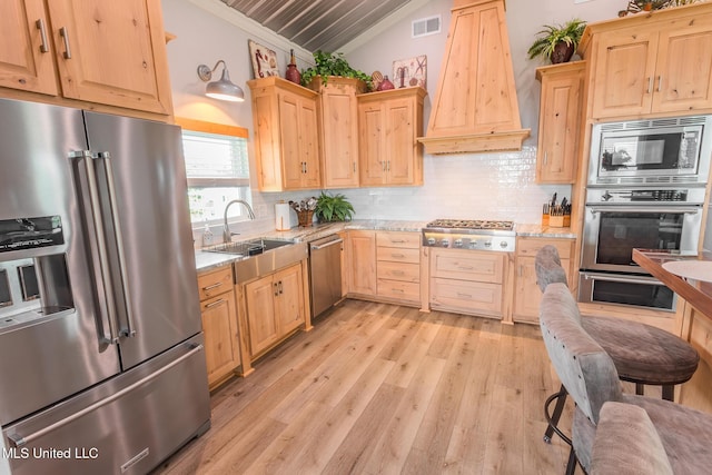 5004 Oak St, Bay Saint Louis, MS 39520 - kitchen featuring stainless steel appliances, custom range hood, light brown cabinetry, vaulted ceiling, and ornamental molding