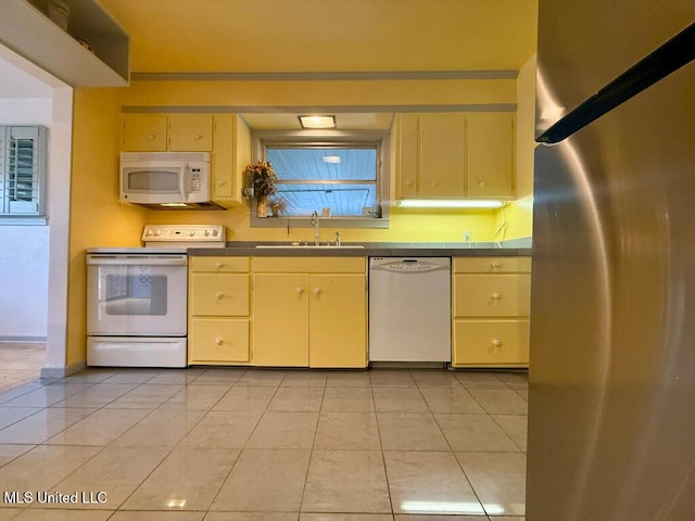 kitchen with a sink, white appliances, light tile patterned flooring, and cream cabinetry