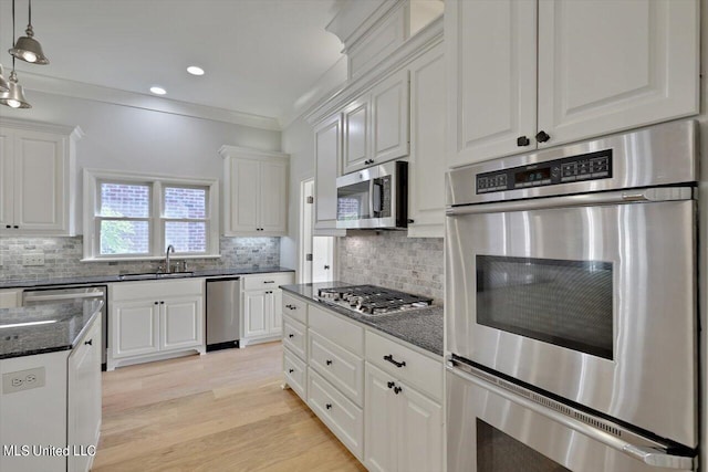 kitchen with ornamental molding, appliances with stainless steel finishes, light wood-type flooring, and white cabinets