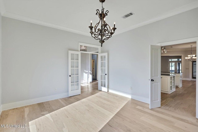 unfurnished dining area with french doors, crown molding, a notable chandelier, and light hardwood / wood-style flooring