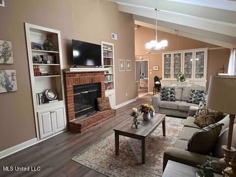 living room with a chandelier, wood-type flooring, a brick fireplace, vaulted ceiling, and built in shelves