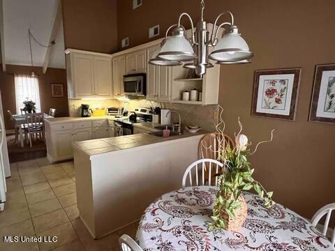 kitchen featuring tile countertops, appliances with stainless steel finishes, open shelves, a peninsula, and a notable chandelier