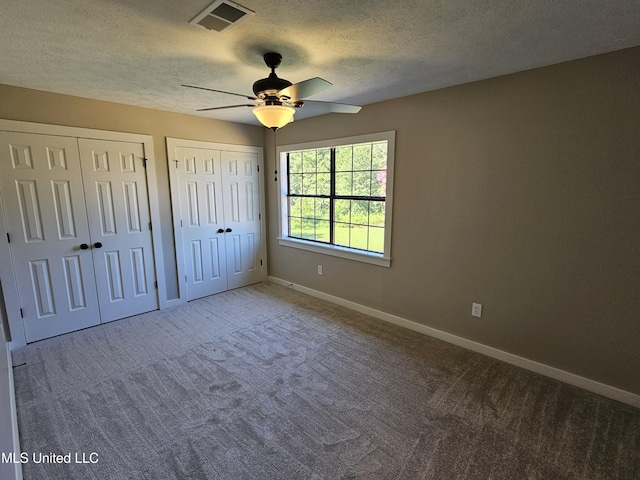 unfurnished bedroom featuring ceiling fan, carpet floors, a textured ceiling, and two closets