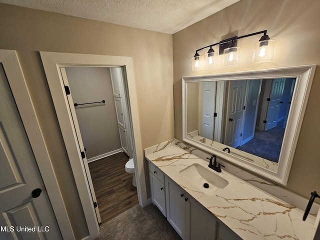 bathroom with toilet, vanity, a textured ceiling, and hardwood / wood-style flooring