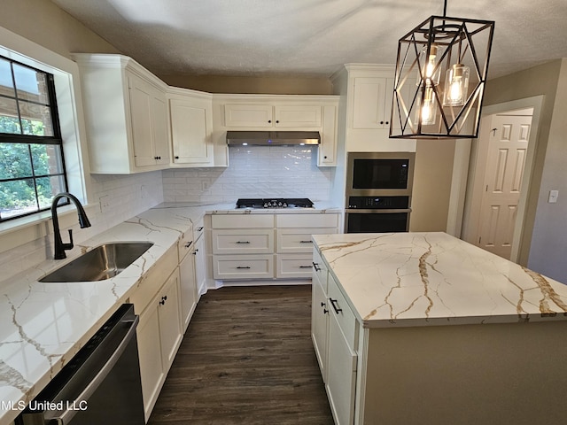 kitchen with appliances with stainless steel finishes, sink, white cabinets, a center island, and hanging light fixtures