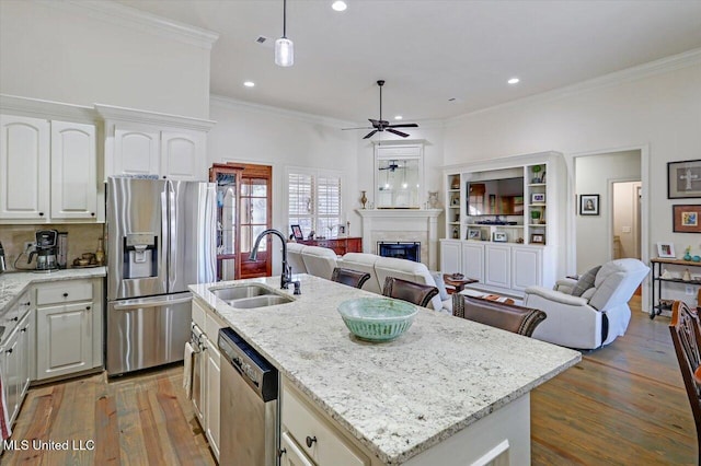 kitchen with a center island with sink, hanging light fixtures, ceiling fan, light stone countertops, and stainless steel appliances