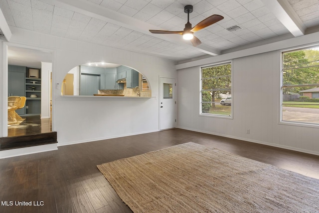 unfurnished living room with a ceiling fan, wood-type flooring, beamed ceiling, and baseboards