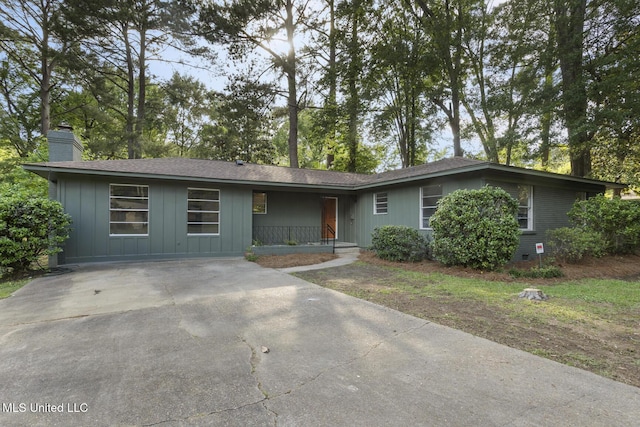 ranch-style home featuring a chimney, board and batten siding, covered porch, and concrete driveway