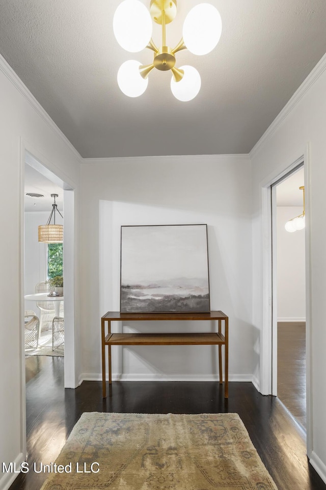 hallway with wood finished floors, crown molding, baseboards, and a chandelier