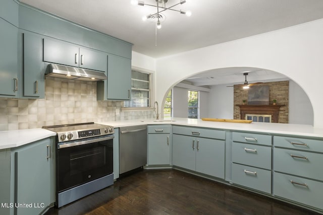 kitchen featuring stainless steel appliances, under cabinet range hood, a sink, decorative backsplash, and arched walkways