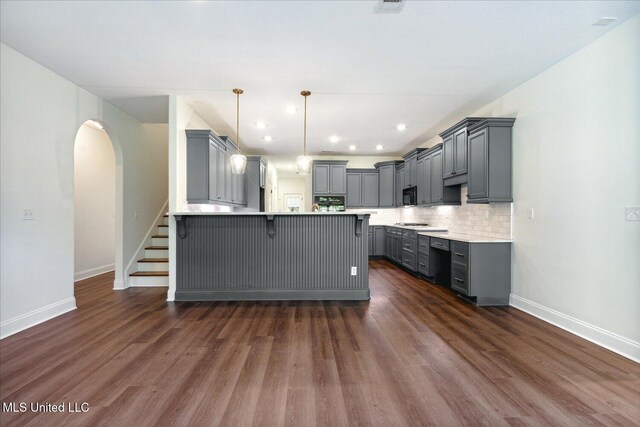 kitchen featuring gray cabinets, tasteful backsplash, dark hardwood / wood-style flooring, a kitchen breakfast bar, and hanging light fixtures