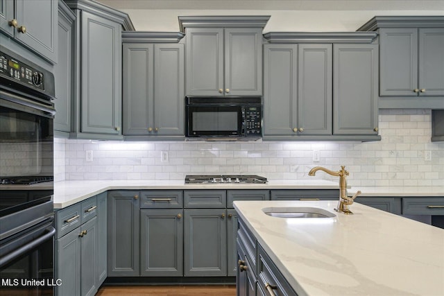 kitchen with gray cabinets, double oven, stainless steel gas stovetop, sink, and light stone countertops