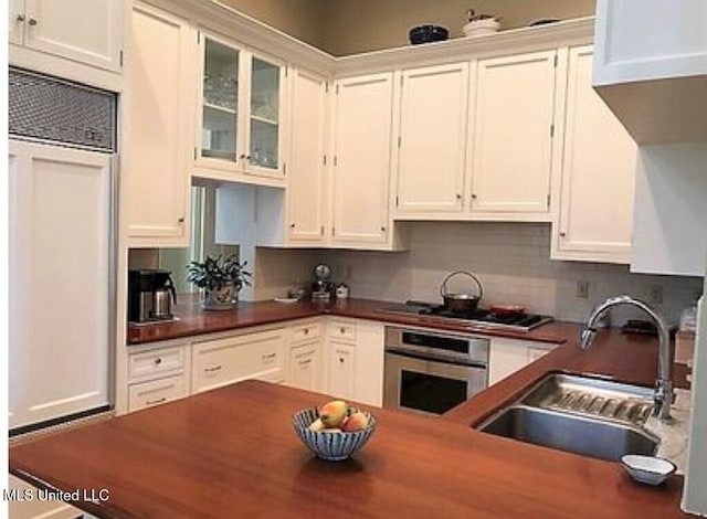 kitchen with white cabinets, decorative backsplash, gas stovetop, sink, and oven