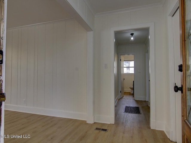 hallway with light wood-style floors, visible vents, crown molding, and baseboards