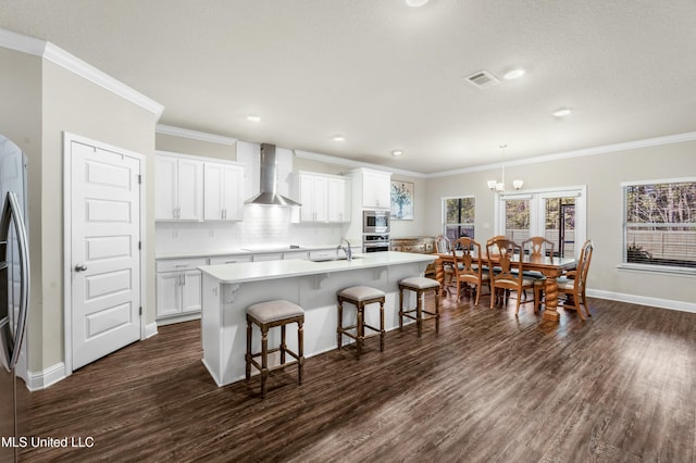 kitchen featuring white cabinets, sink, decorative light fixtures, and wall chimney range hood