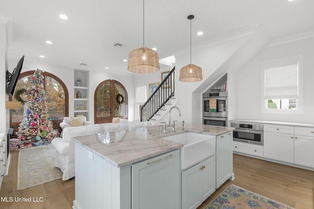 kitchen with light stone counters, sink, decorative light fixtures, a center island with sink, and white cabinetry