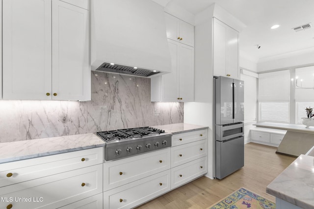 kitchen with premium range hood, white cabinets, tasteful backsplash, light stone counters, and stainless steel gas cooktop