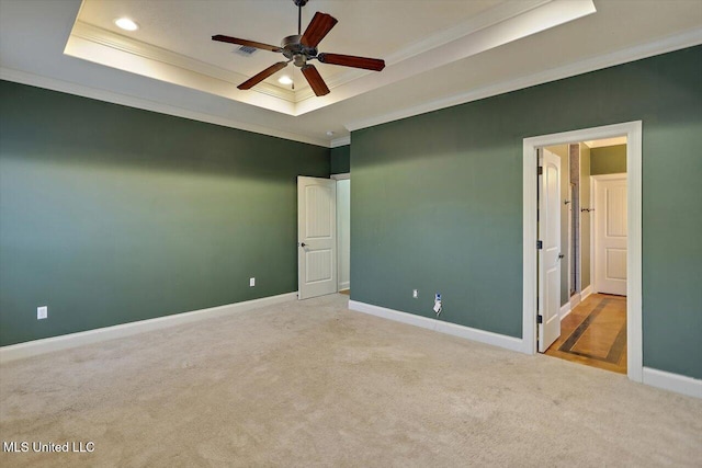 carpeted spare room featuring a raised ceiling, ceiling fan, and ornamental molding