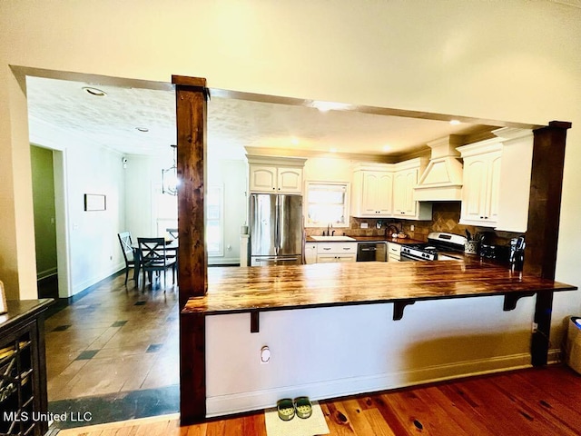 kitchen featuring premium range hood, dark wood-type flooring, white cabinets, kitchen peninsula, and stainless steel appliances