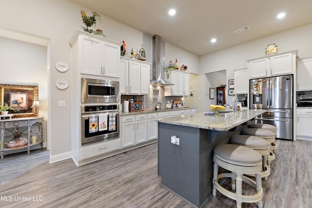 kitchen featuring appliances with stainless steel finishes, wall chimney exhaust hood, tasteful backsplash, light wood-style floors, and recessed lighting