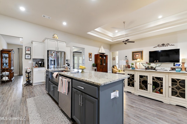 kitchen featuring appliances with stainless steel finishes, a ceiling fan, white cabinetry, light wood-style flooring, and a center island with sink