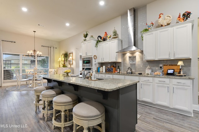 kitchen featuring wall chimney range hood, light wood-style flooring, tasteful backsplash, white cabinets, and recessed lighting