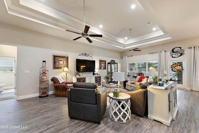 living room with a tray ceiling, a ceiling fan, ornamental molding, wood finished floors, and recessed lighting