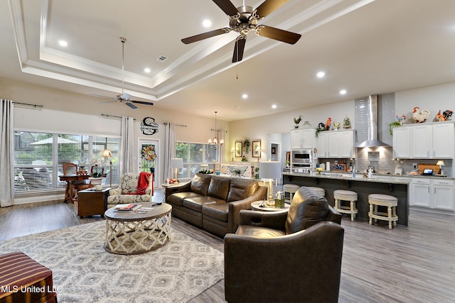 living area with ceiling fan, healthy amount of natural light, ornamental molding, a tray ceiling, and wood finished floors