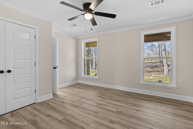 empty room with visible vents, crown molding, light wood-style flooring, and baseboards