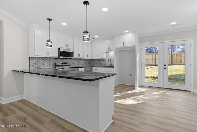 kitchen featuring stainless steel appliances, dark countertops, white cabinets, light wood-type flooring, and a peninsula