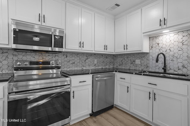 kitchen with stainless steel appliances, dark countertops, visible vents, white cabinetry, and a sink