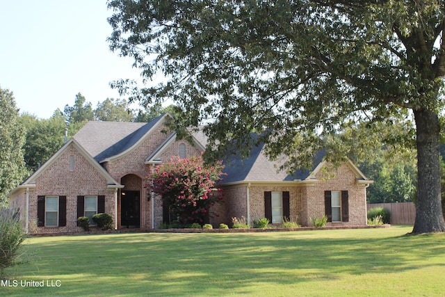 view of front of house featuring roof with shingles, fence, a front lawn, and brick siding