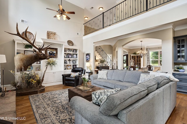 living area with arched walkways, ornamental molding, a chandelier, wood finished floors, and stairway