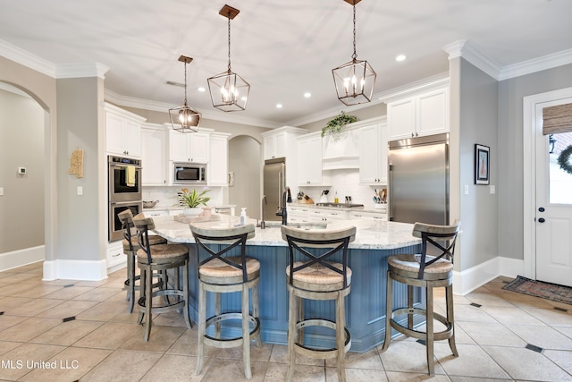 kitchen featuring built in appliances, arched walkways, backsplash, white cabinets, and crown molding