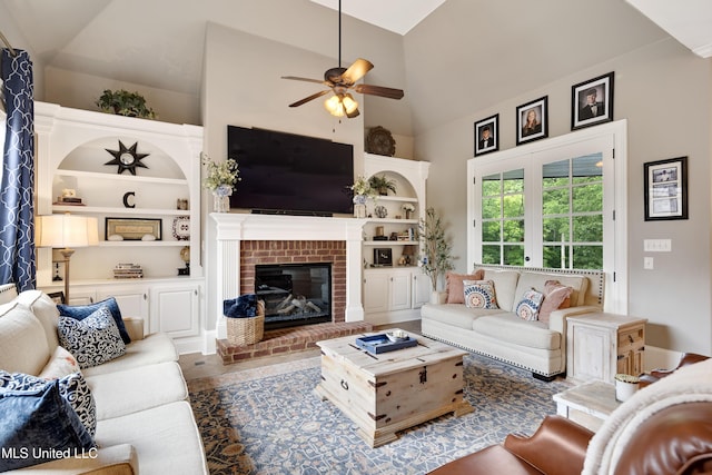 living area featuring a ceiling fan, a fireplace, built in shelves, and high vaulted ceiling