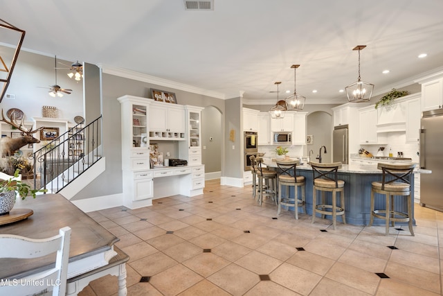kitchen featuring appliances with stainless steel finishes, a breakfast bar, a ceiling fan, white cabinets, and ornamental molding