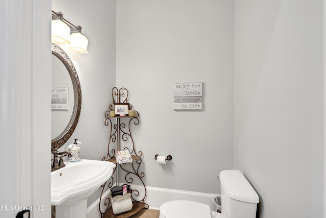 half bath with toilet, a sink, and baseboards