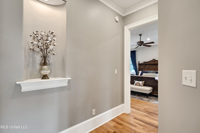 corridor featuring wood finished floors, ornamental molding, and baseboards