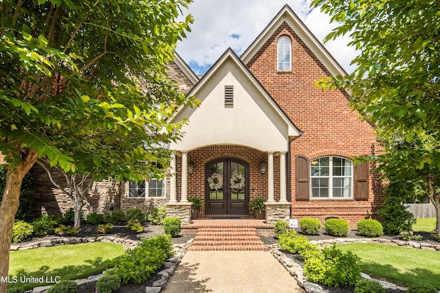 property entrance featuring french doors, brick siding, stucco siding, stone siding, and a lawn