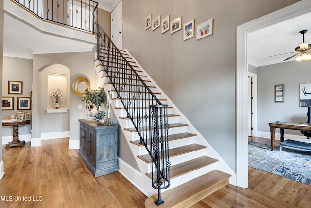stairs featuring arched walkways, ceiling fan, wood finished floors, ornamental molding, and baseboards