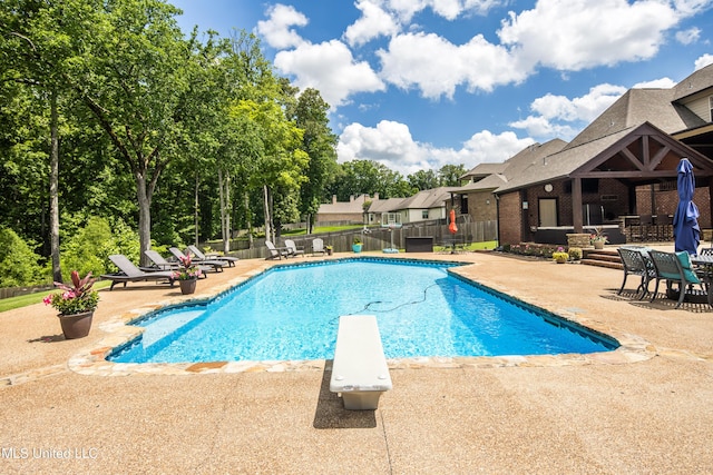 view of swimming pool featuring a patio, fence, and a diving board