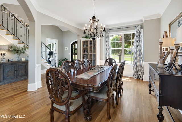 dining space with arched walkways, light wood-style flooring, stairway, a chandelier, and ornamental molding