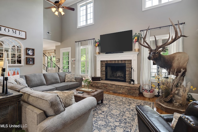 living room with wood finished floors, a ceiling fan, stairway, a high ceiling, and a stone fireplace