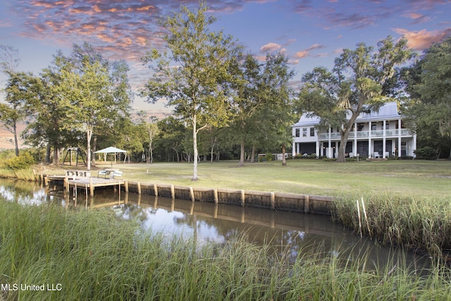 view of dock featuring a lawn, a water view, and a balcony