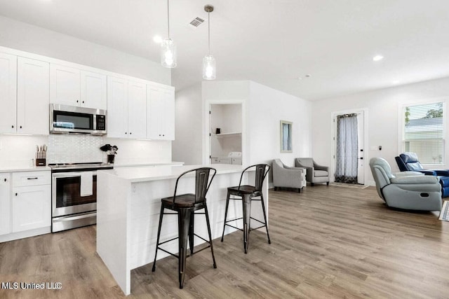 kitchen with white cabinetry, stainless steel appliances, pendant lighting, a breakfast bar, and light wood-type flooring